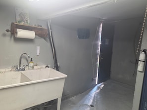 A bathroom with a sink, a toilet, a shower, and a whiteboard on the wall.