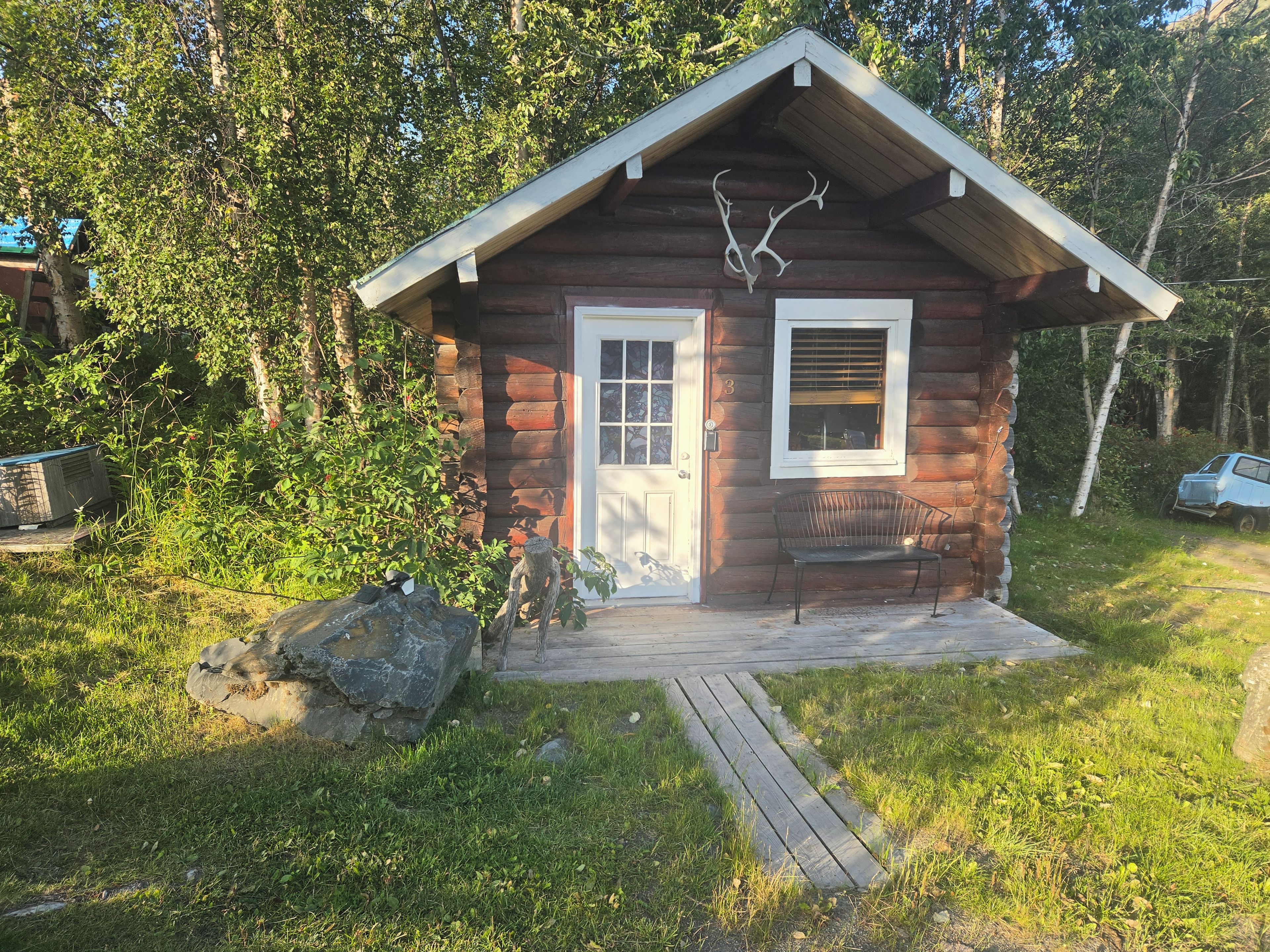 Eine kleine Holzhütte mit einer Holzveranda, einer Bank und aufgehängten Geweihen an der Wand.