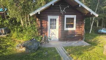 Eine kleine Holzhütte mit einer Holzveranda, einer Bank und aufgehängten Geweihen an der Wand.