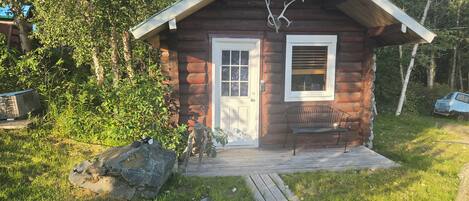 A small log cabin with a wooden porch, a bench, and antlers mounted on the wall.