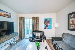 A living room with a TV, a sofa, a chair, and a painting on the wall. - Serene 1-bedroom apartment with AC in vibrant Dallas pool washer & Dryer, Wifi (Dallas)