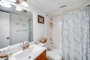 Casa de banho com lavatório branco, espelho, sanita e zona de duche.