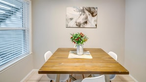 Zona pranzo con tavolo in legno, sedie bianche, un vaso di fiori e un quadro raffigurante un cavallo.