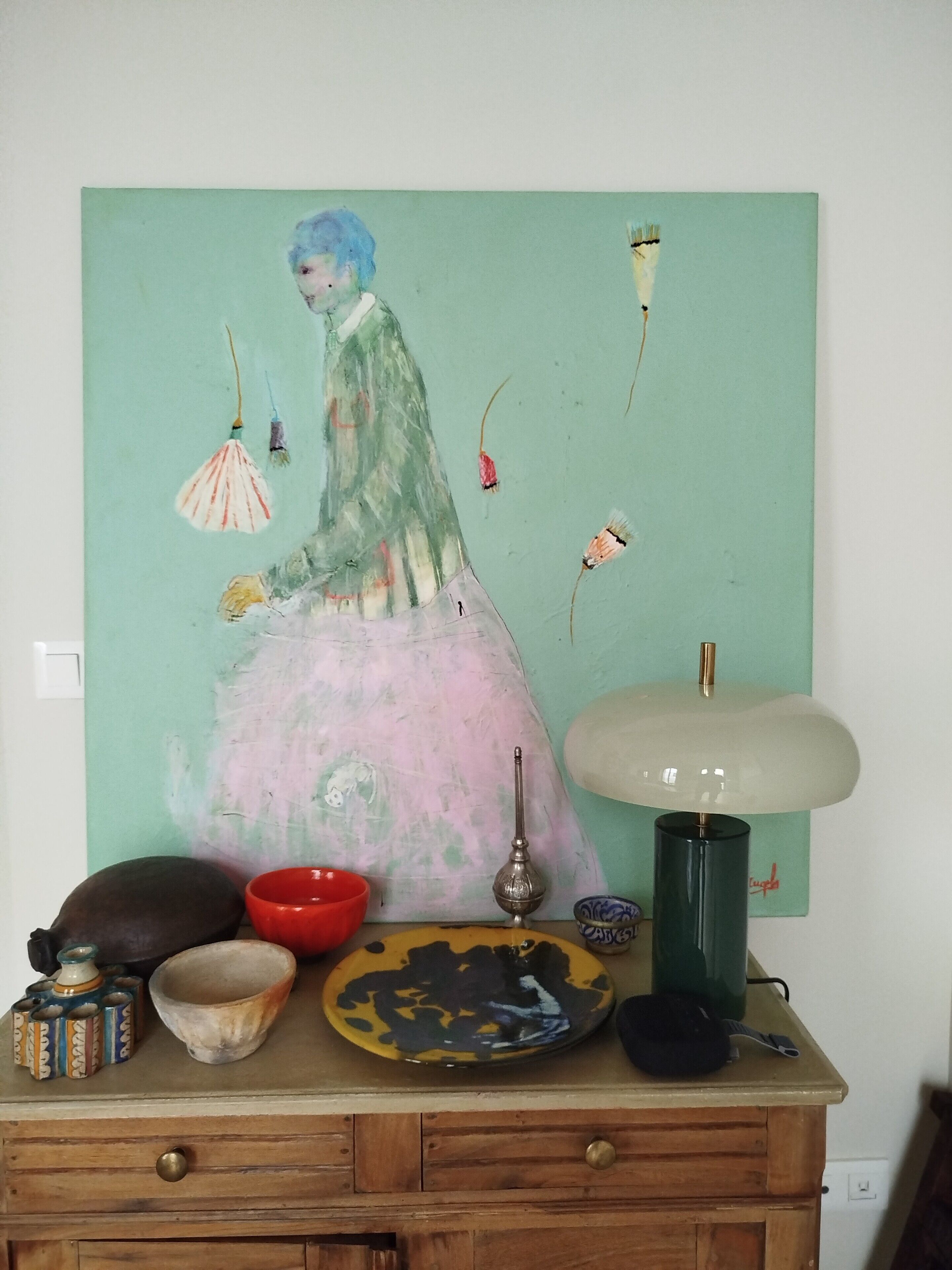 Une pièce comprenant une commode en bois, une table ornée de divers objets décoratifs et un tableau accroché au mur.