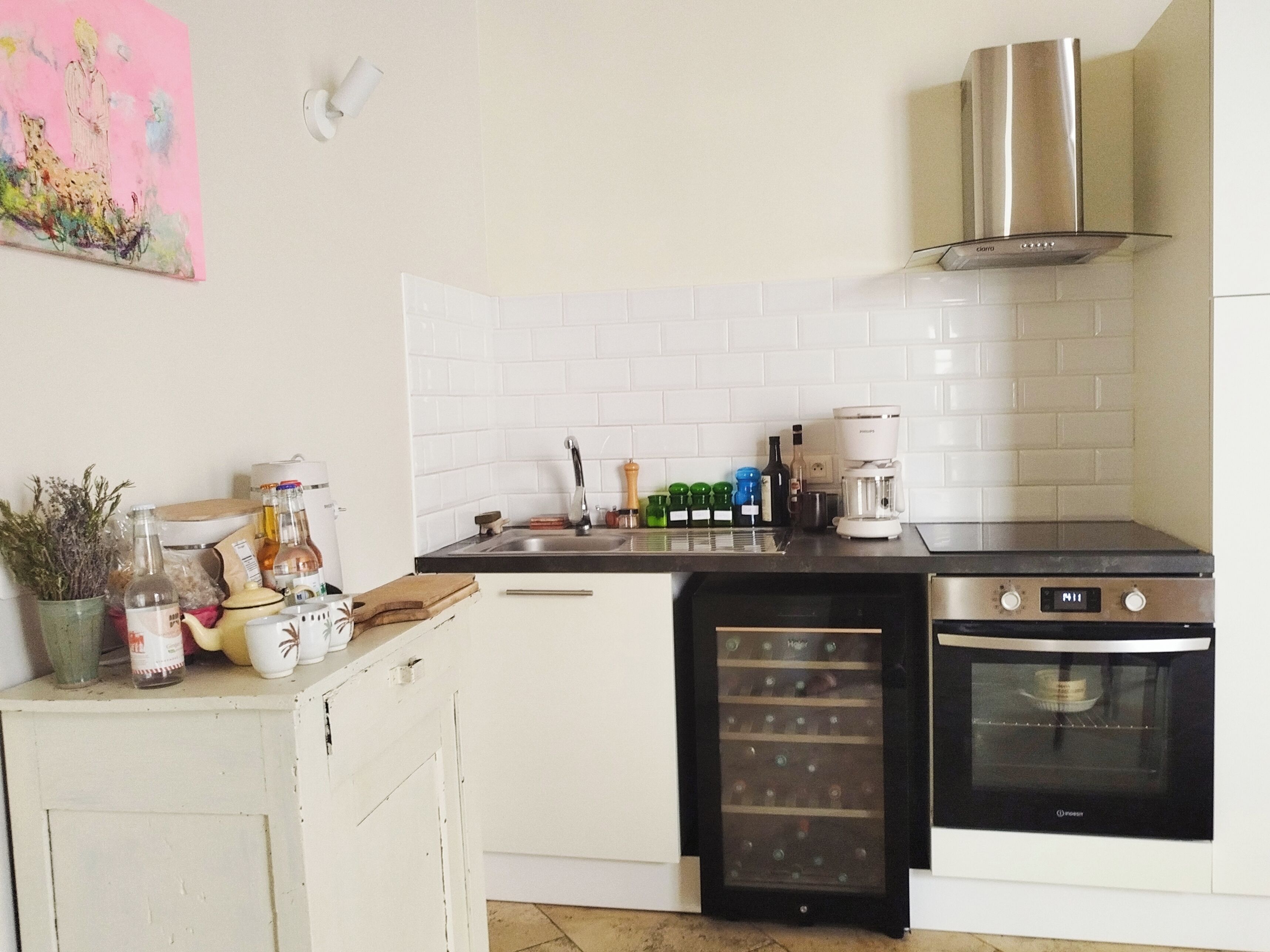 Une cuisine avec des carreaux blancs, une hotte de cuisine en acier inoxydable, un four encastré et une machine à café.