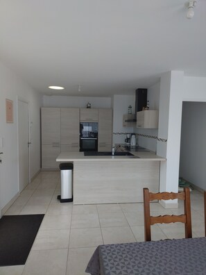 A modern kitchen with a central island, a dining area with a table, and a trash bin. - House on a quiet street near the beaches (Bénodet)