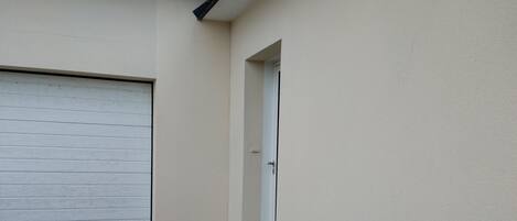 A garage with a white door, a wooden ramp leading to a driveway, and a small step leading to a door.