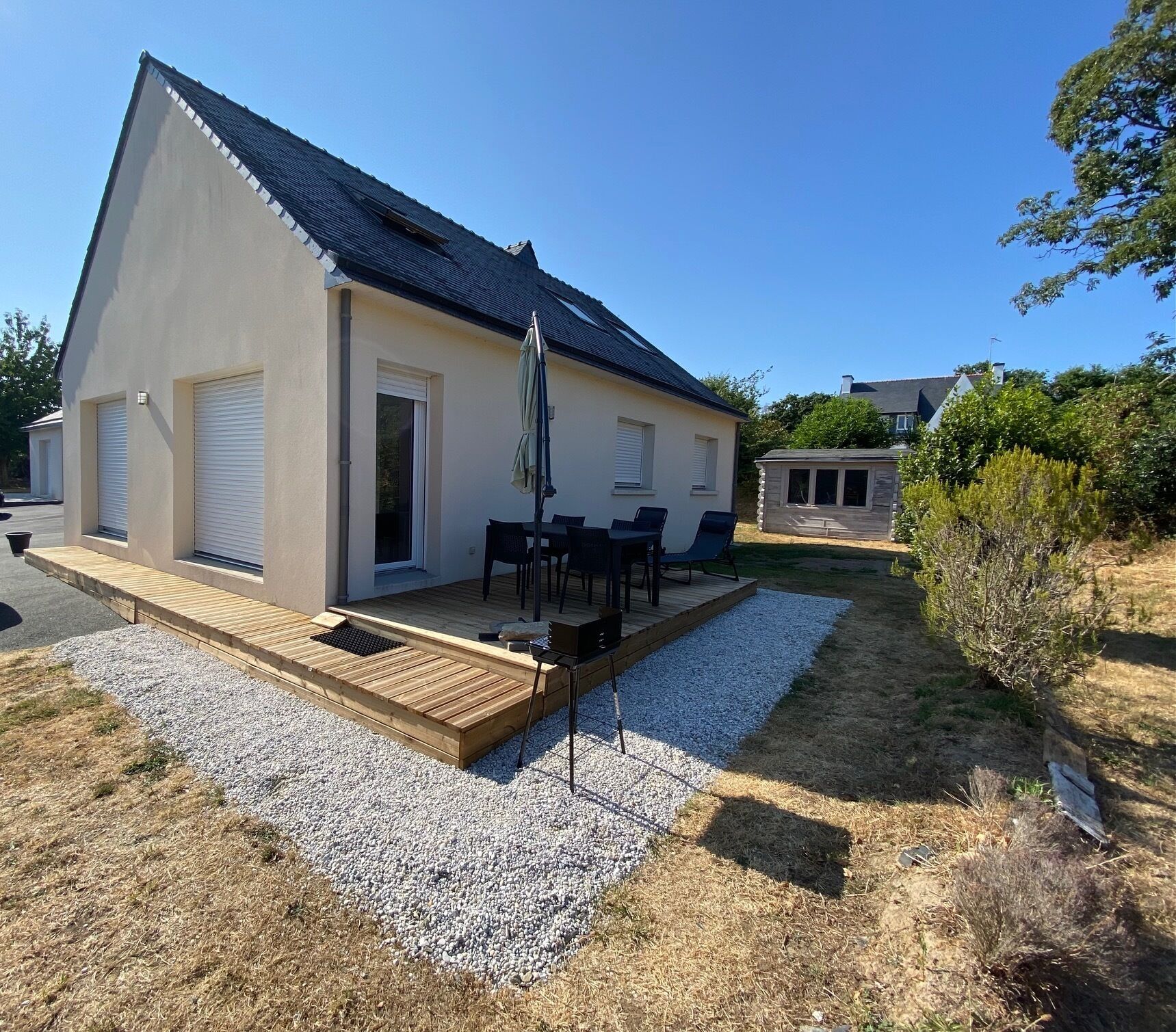 Ein modernes Haus mit überdachter Terrasse, einer kleinen Holzterrasse und einem Schotterweg.