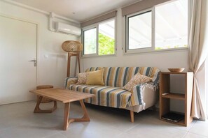 A living room with a sofa, a wooden table, a wicker floor lamp, and a small wooden shelf.