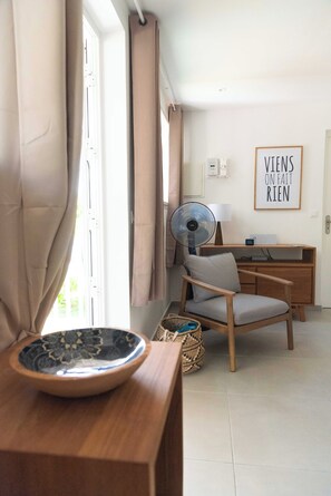 Une pièce comprenant un bureau en bois, une chaise, un ventilateur, un luminaire fixé au mur et un panneau encadré.