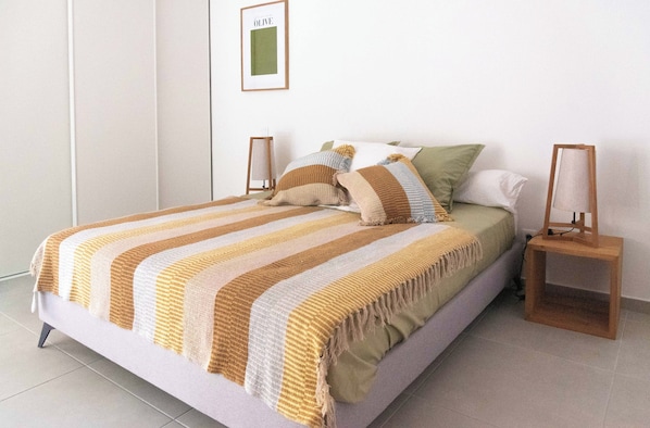 A neatly made bed with striped bedding, a framed picture on the wall, and a bedside table with a lamp.