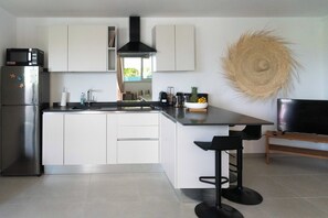 Une cuisine moderne avec des armoires blanches, un réfrigérateur en acier inoxydable, un micro-ondes noir, une cuisinière noire, un tabouret de bar noir et un téléviseur posé sur un meuble en bois.