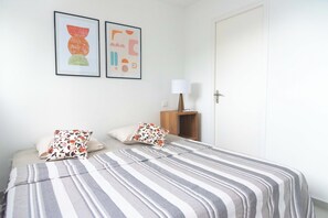 Une chambre à coucher avec un lit, des oreillers, une table de chevet, une lampe et deux œuvres d’art encadrées accrochées au mur.