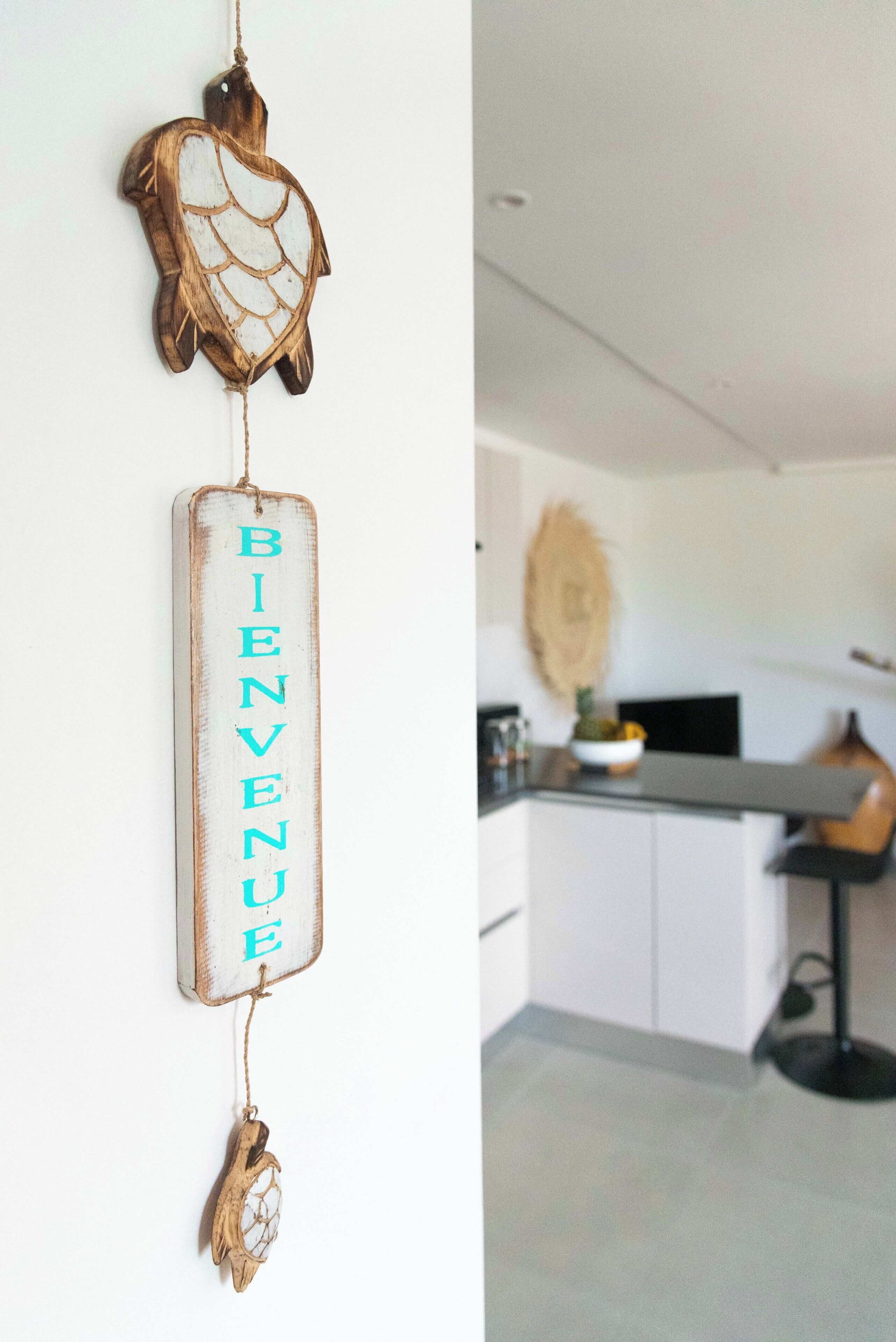 A kitchen with a white countertop, a hanging decorative piece, and a hanging sign with the word 'BIENVENUE'.