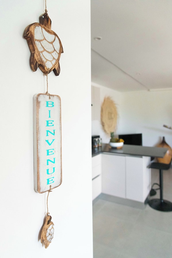 A kitchen with a white countertop, a hanging decorative piece, and a hanging sign with the word 'BIENVENUE'.