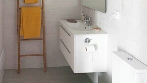 Un bagno con un lavandino bianco, uno specchio, un water e una scala in legno con asciugamani.