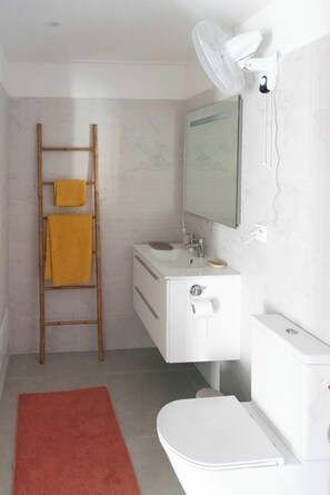 Ein Badezimmer mit weißem Waschbecken, Spiegel, Toilette und einer Holzleiter mit Handtüchern.