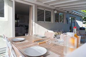 Un espace extérieur aménagé pour les repas, avec une table pour quatre personnes, un barbecue et une vue sur la maison.
