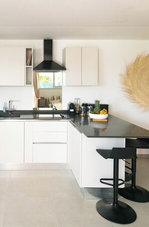 A modern kitchen with white cabinetry, a black countertop, and a central island with bar stools.