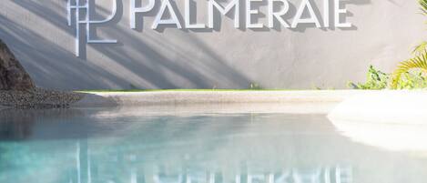 Una piscina cristalina con el reflejo del nombre del hotel 'PALMERAEI' en la pared.