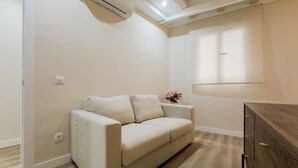Sofá em tons neutros em um quarto com um armário de madeira e um ar condicionado fixado na parede.
