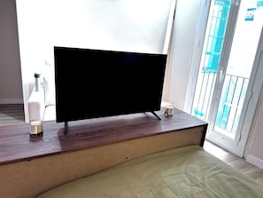 A flat-screen TV on a wooden stand in a room with a window and a balcony. - Two-bedroom apartment in downtown Barcelona 2-2 (Barcelona)