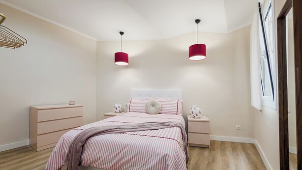 Quarto com cama, duas mesas de cabeceira, luminária pendente e janela com cortinas.