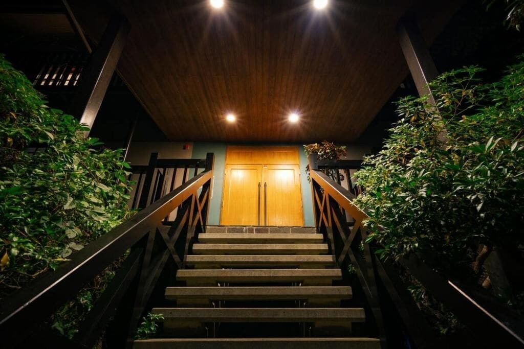 Una escalera conduce a una puerta de madera, con barandales metálicos a ambos lados.