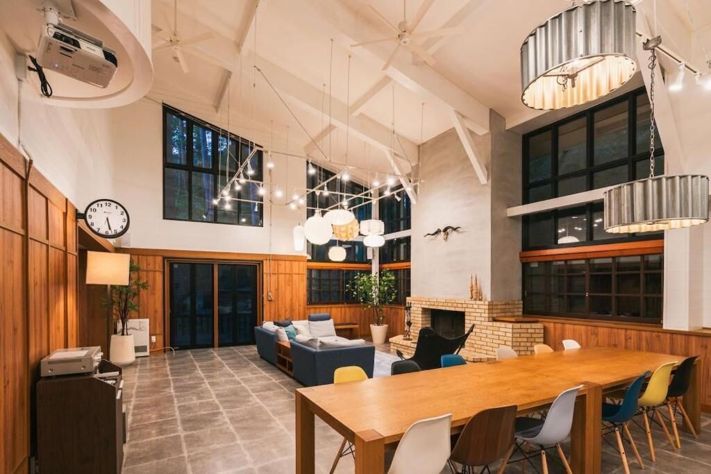Een ruime kamer met een grote houten eettafel, meerdere stoelen, een open haard en hangende lampen.