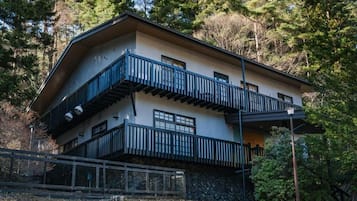 Un edificio de dos pisos con un balcón en el nivel superior, rodeado de árboles.