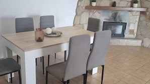 Uma área de refeições com parede de pedra, lareira e mesa moderna com cadeiras.