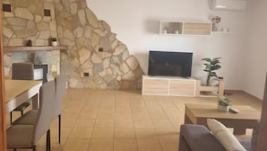 Uma sala de estar com parede de pedra, TV de tela plana, mesa de centro de madeira e um sofá.