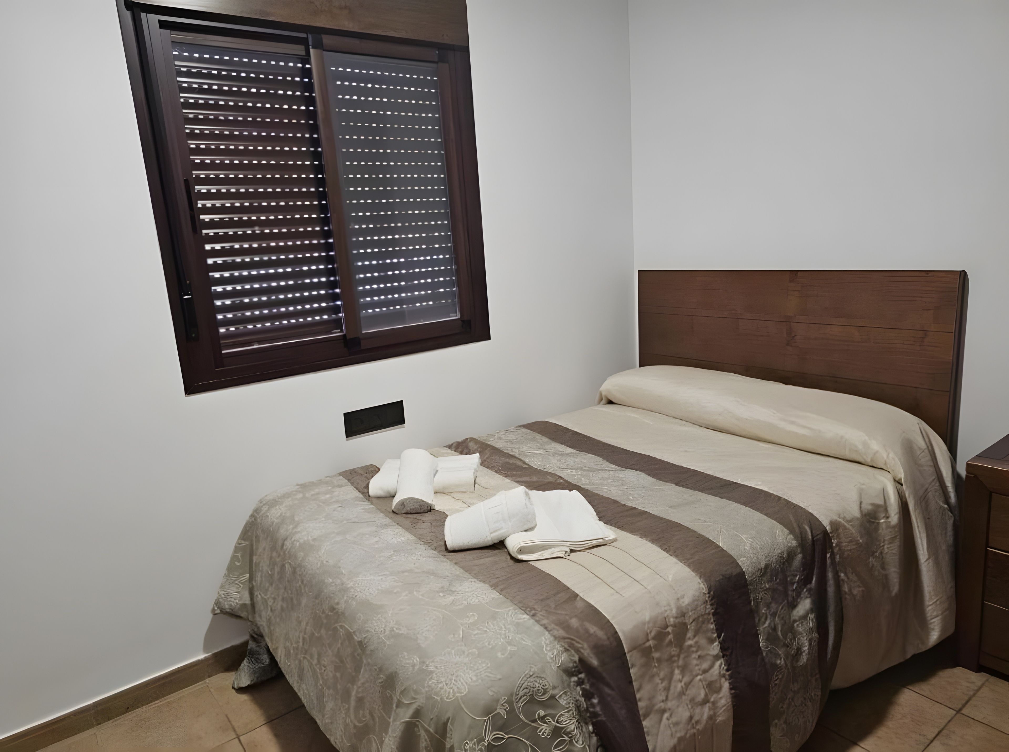 A bedroom with a bed, a window with blinds, and a bedside table.