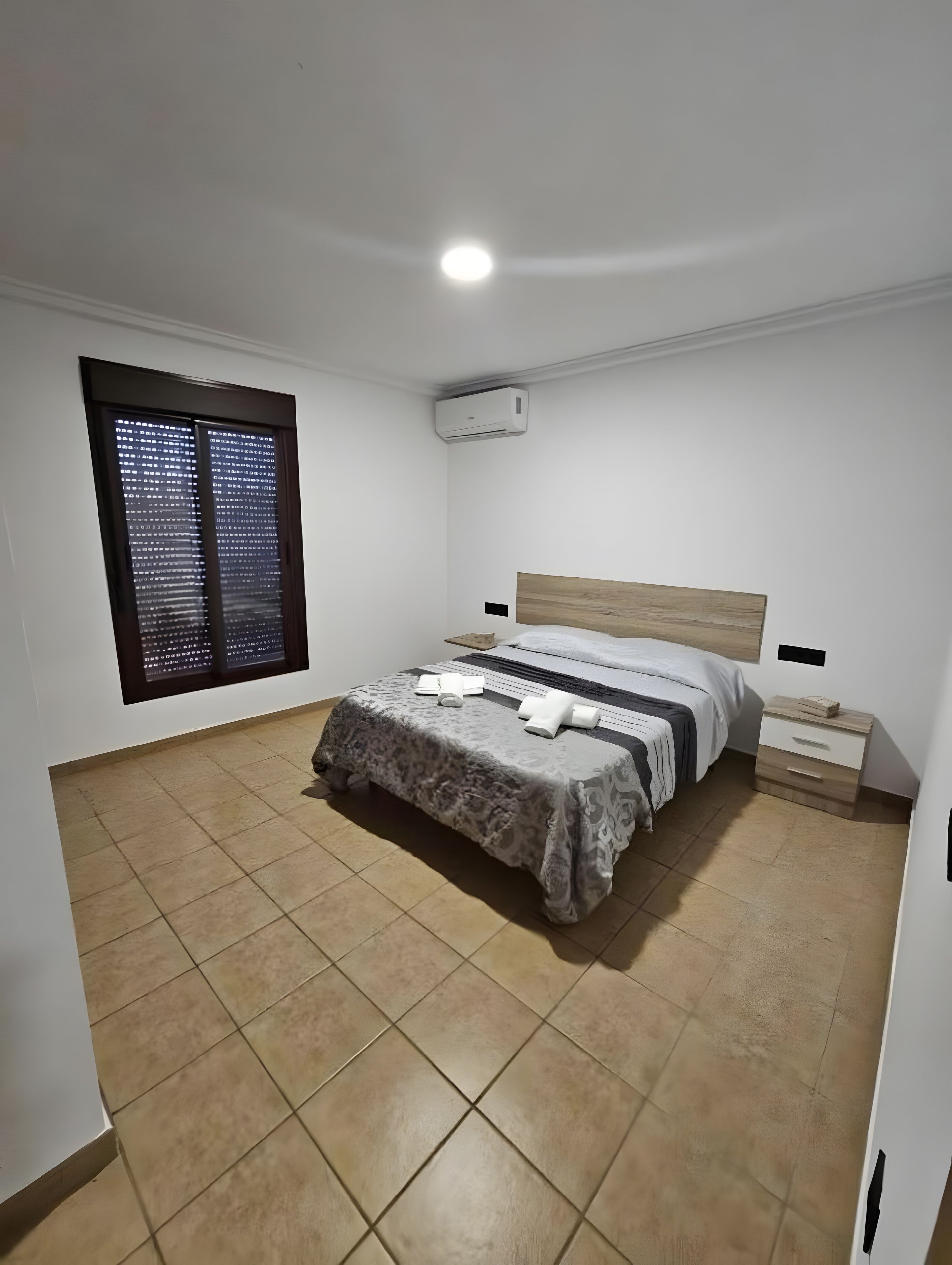Una camera da letto con un letto, comodini, un condizionatore d'aria e una finestra con persiane.