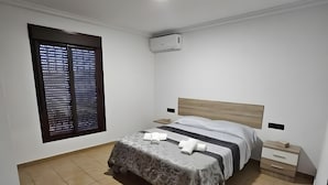 Quarto com cama, mesas de cabeceira, ar condicionado e janela com persianas.