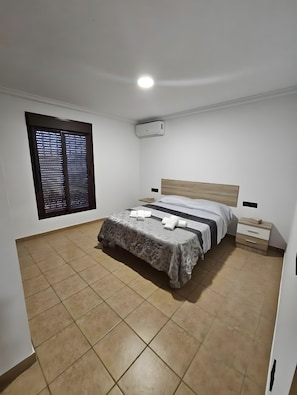 Una camera da letto con un letto, comodini, un condizionatore d'aria e una finestra con persiane.