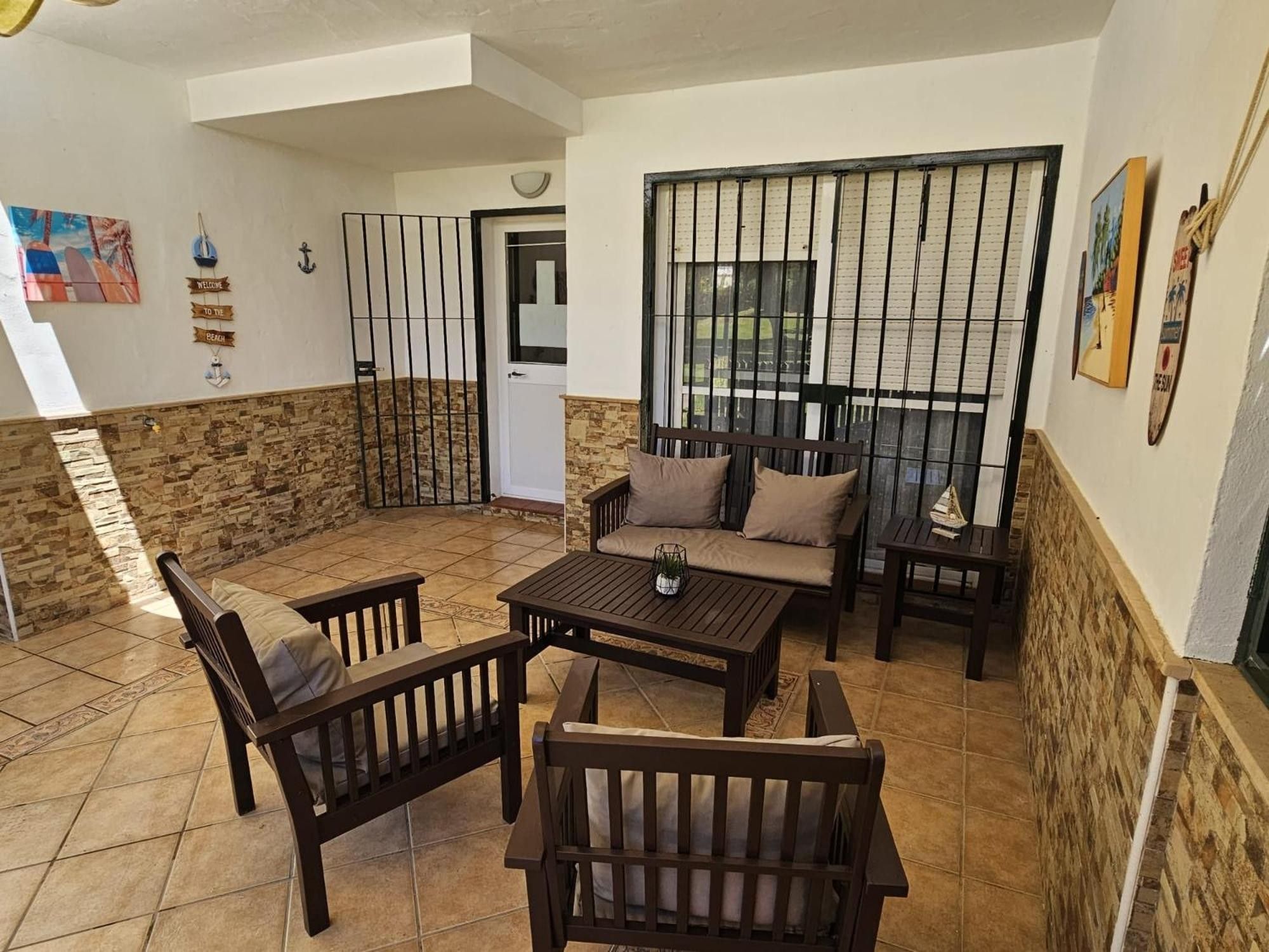Un patio con un muro de piedra, una mesa de madera, dos sofás y una reja de metal.