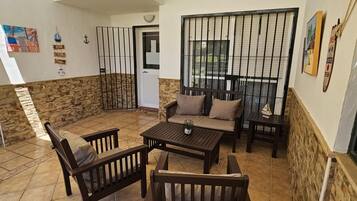 Un patio con un muro de piedra, una mesa de madera, dos sofás y una reja de metal.