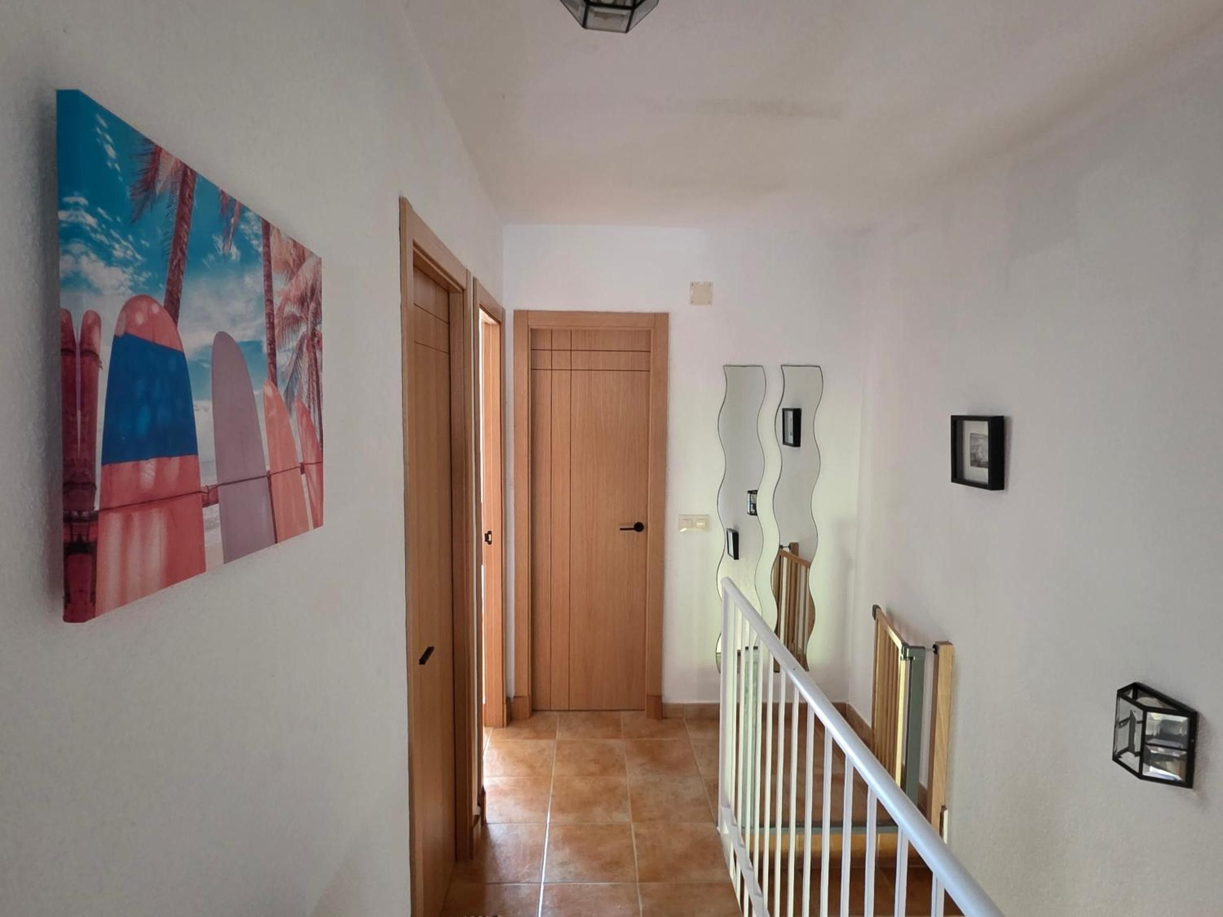 Un pasillo con puerta de madera, suelo de baldosas y una lámpara fijada a la pared.
