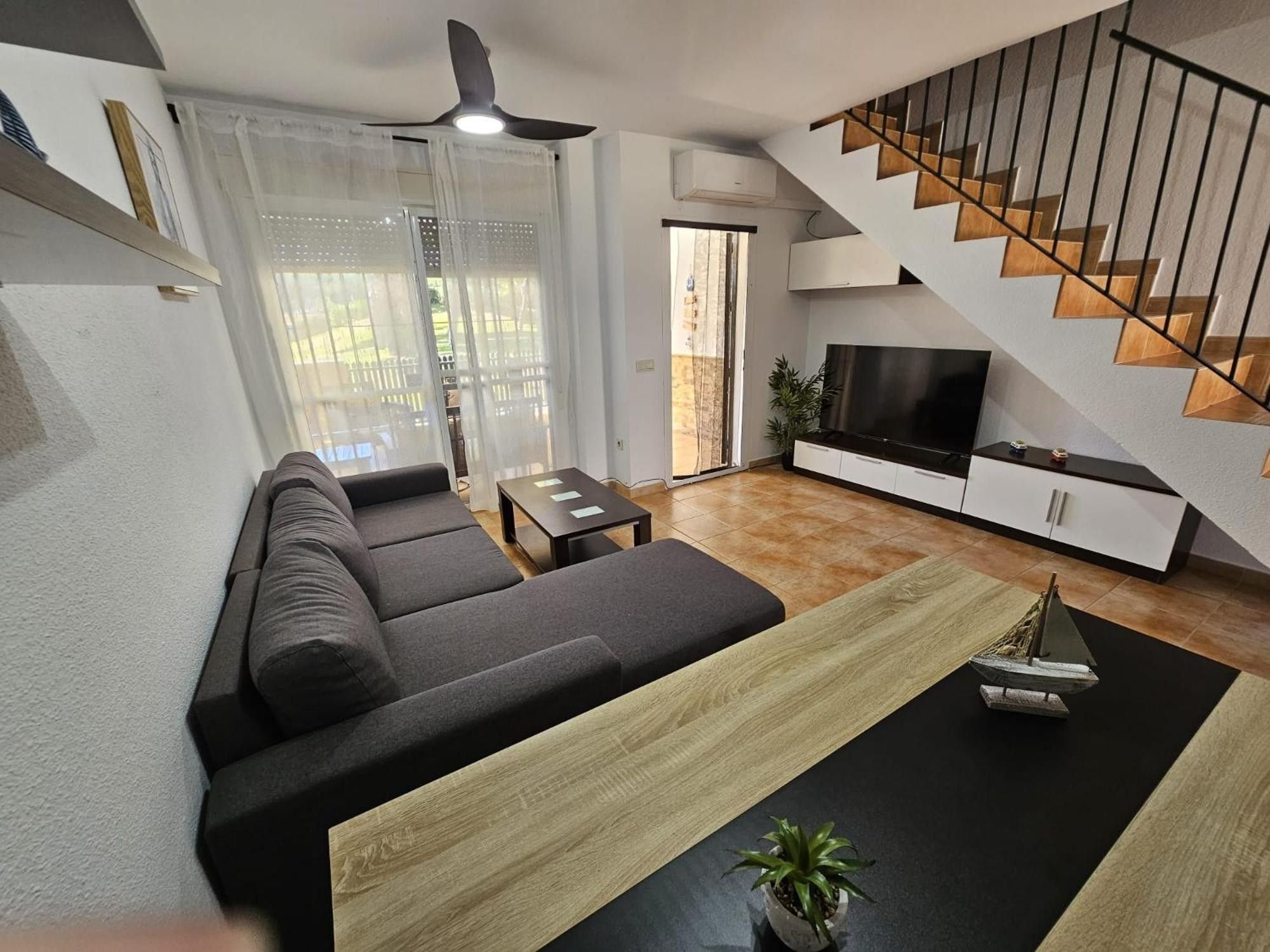 Una sala de estar moderna con sofá, mesa de centro, televisor y escalera.