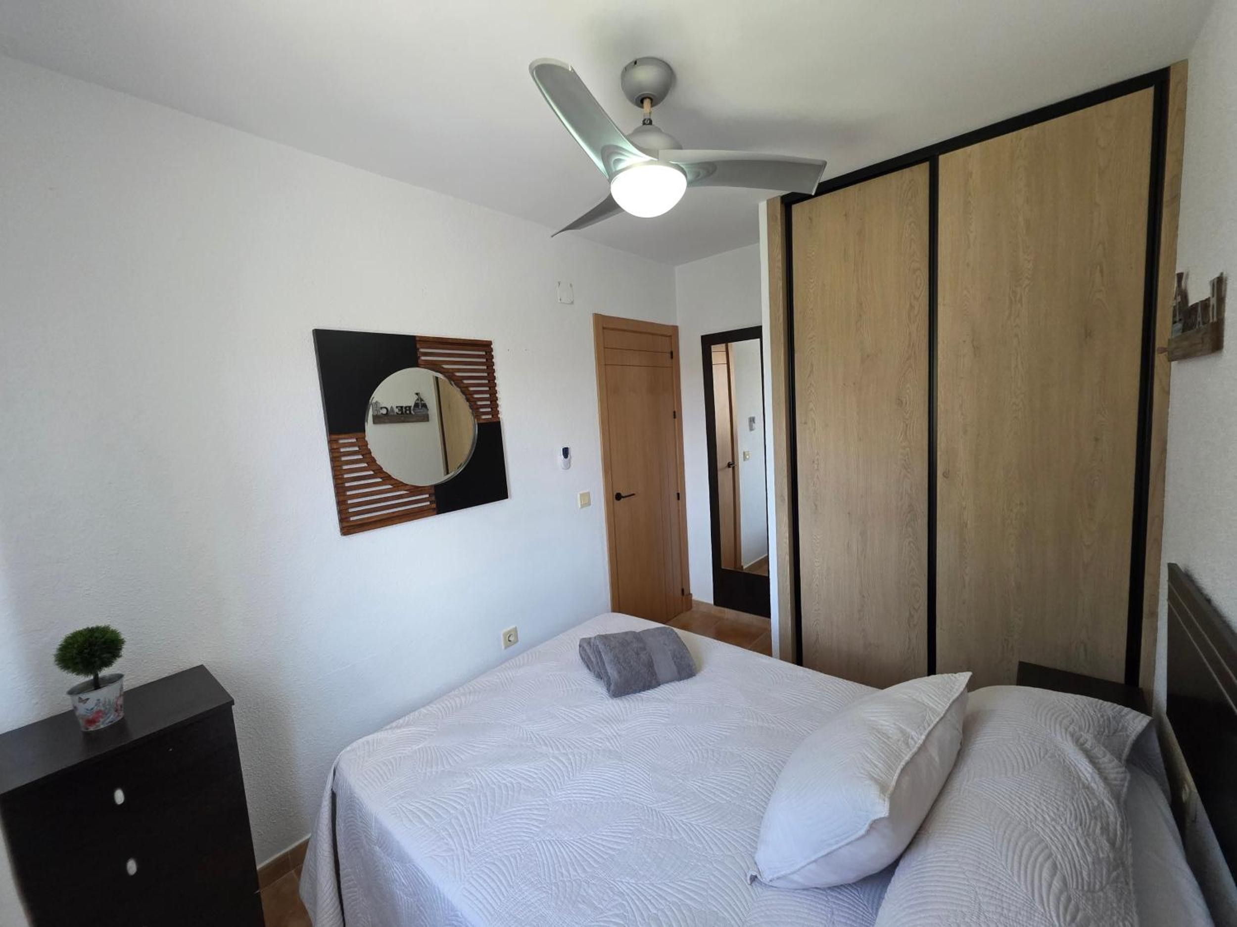 Un dormitorio con cama, ventilador de techo, espejo y armario.