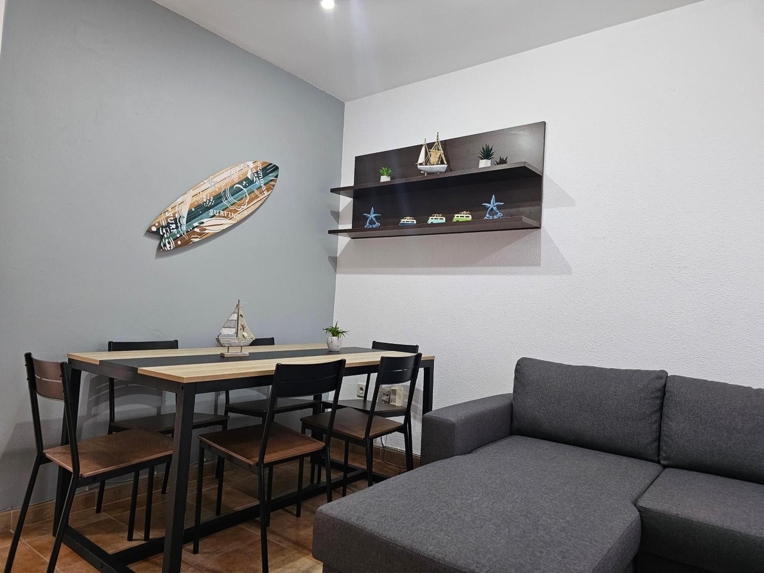 Un espacio moderno con zona de comedor, un sofá gris y objetos decorativos en un estante.