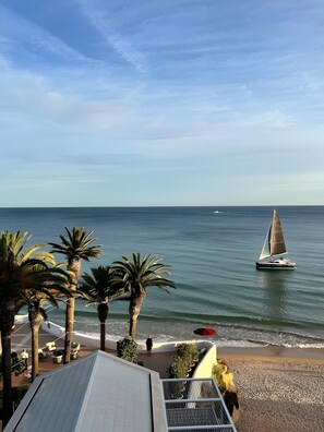 Una playa con palmeras, un velero y un edificio con techo inclinado.