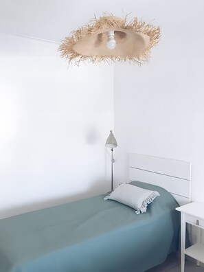 Una cama individual con colchón color turquesa, almohada blanca y mesita de noche blanca.