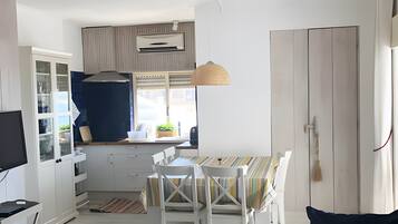 Cuina compacta amb armaris blancs, una taula de dinar amb mantell rayat i una làmpada penjant.