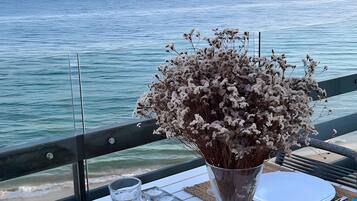 Taula posta amb plats, coberts i espelmes, amb vista a un mar tranquil.