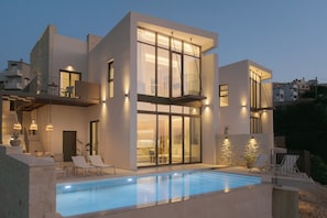 Una casa moderna de dos pisos con piscina, mobiliario exterior y un balcón.