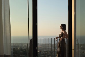 Eine Person steht an einem Balkon mit Blick auf eine Stadtansicht.