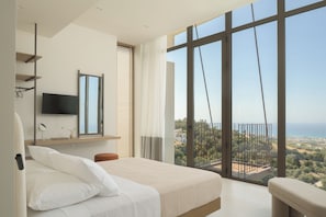Un dormitorio con un ventanal grande, una cama, un televisor montado y vistas a un paisaje.