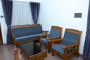 Ett rum med en soffa, två fåtöljer, ett soffbord i glas och gardiner.
